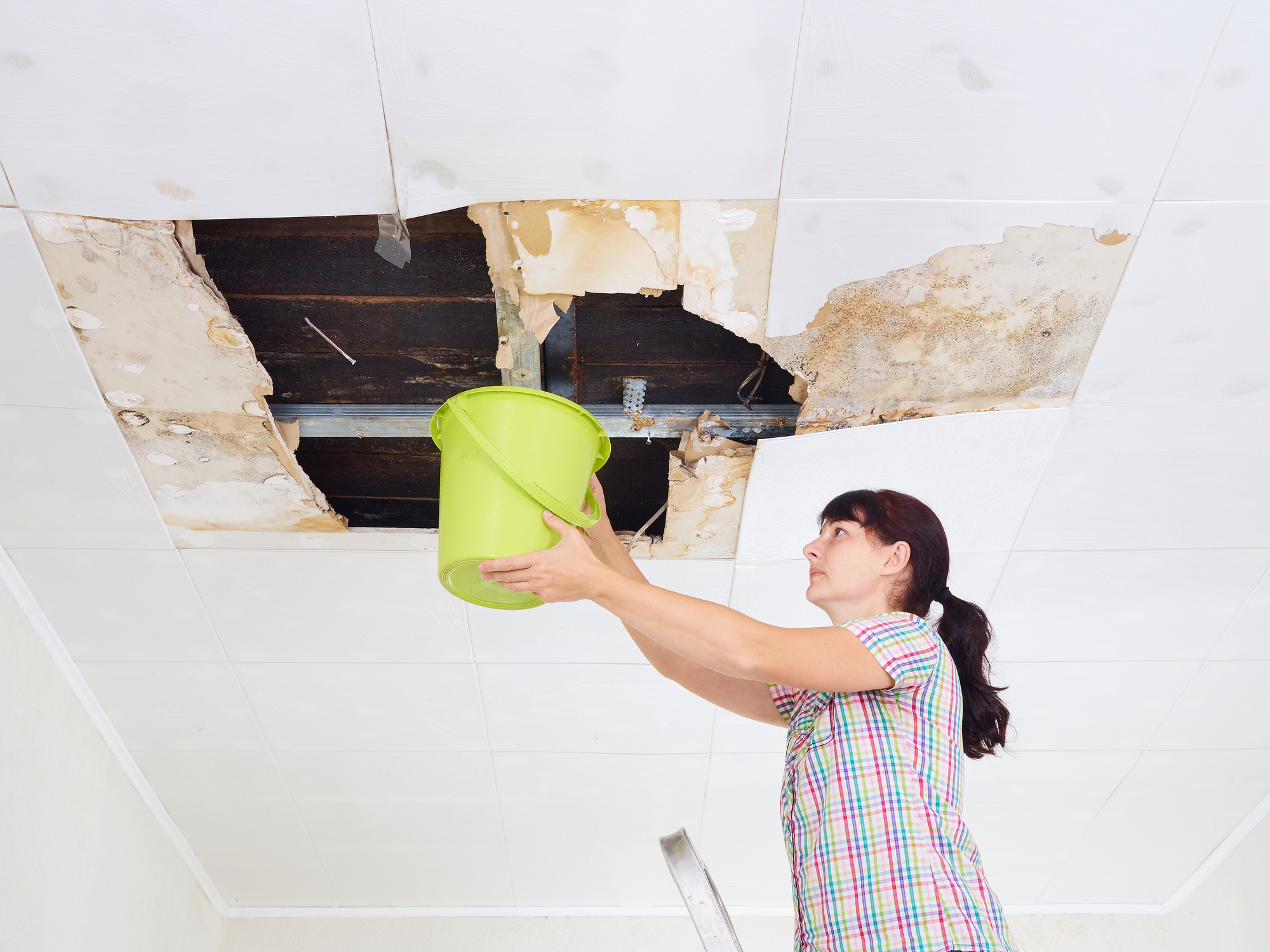 Young woman collecting water from a damaged ceiling