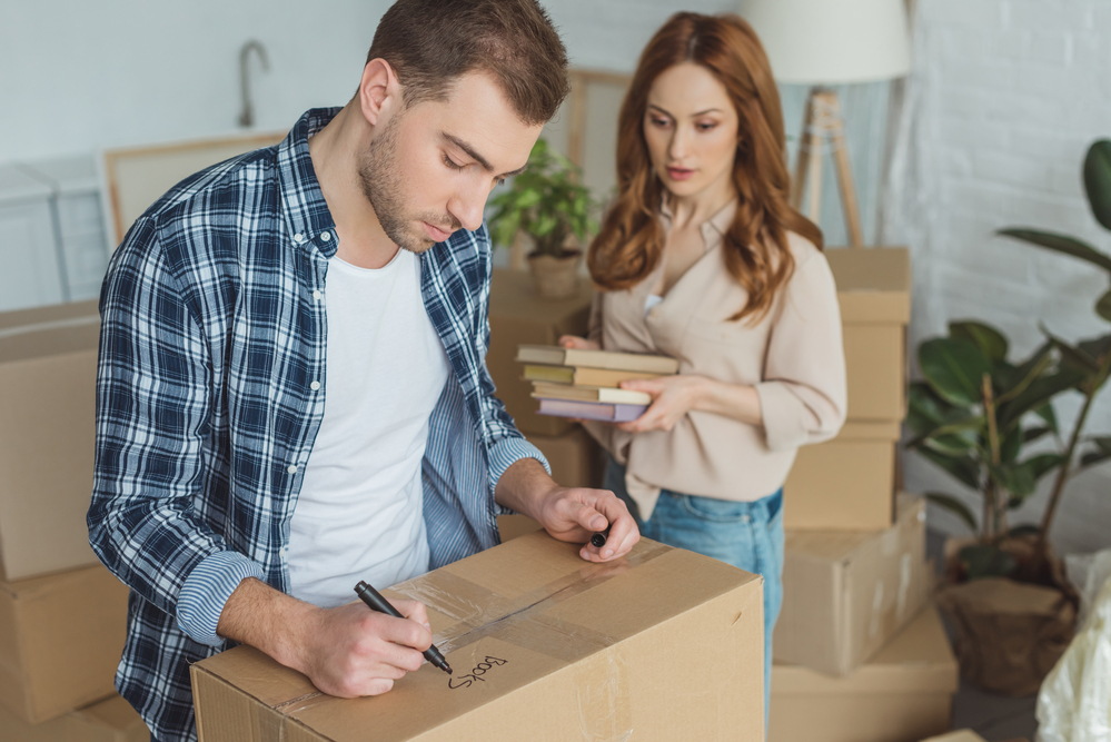 Woman holding books in her hands and man writing something on a box